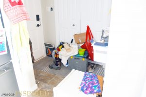 Small entryway with closed doors. The floor is filled with clutter. Mini fridge in the foreground with outwear on top.